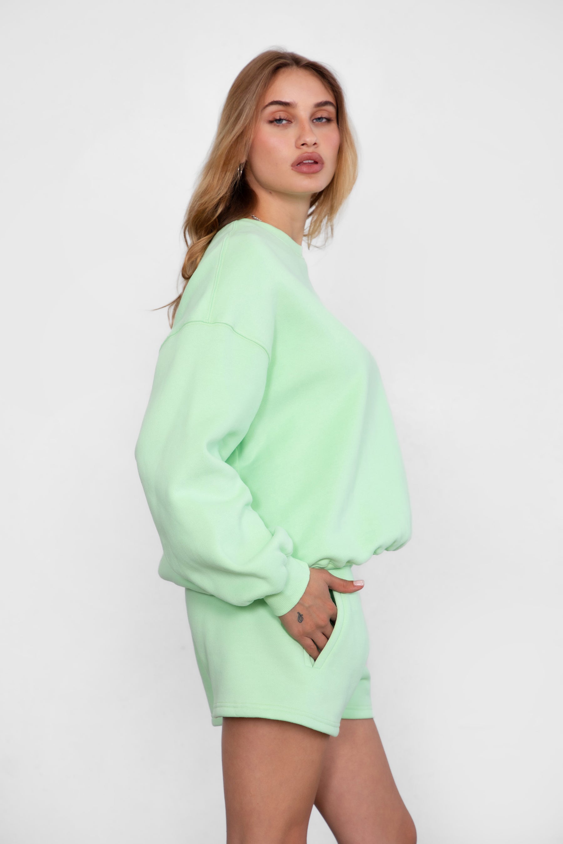 Woman wearing the TIC TOC TH28243 VARSITY pastel lime fleece crew neck pullover sweatshirt featuring dropped shoulders, ribbed trim, and plush fleece fabric with the matching bottoms 