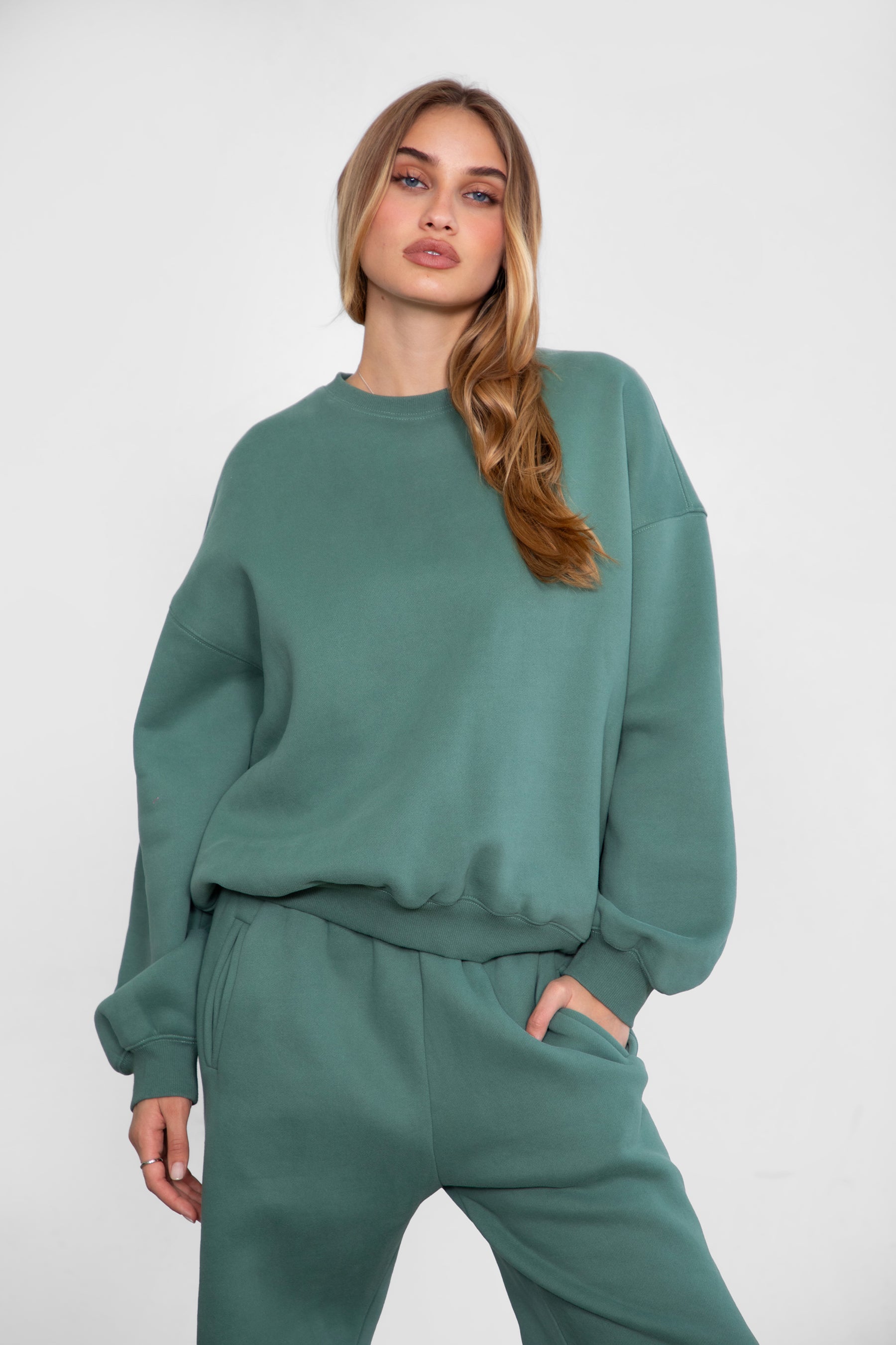 Woman wearing the TIC TOC TH28243 VARSITY pine green fleece crew neck pullover sweatshirt featuring dropped shoulders, ribbed trim, and plush fleece fabric with the matching bottoms 
