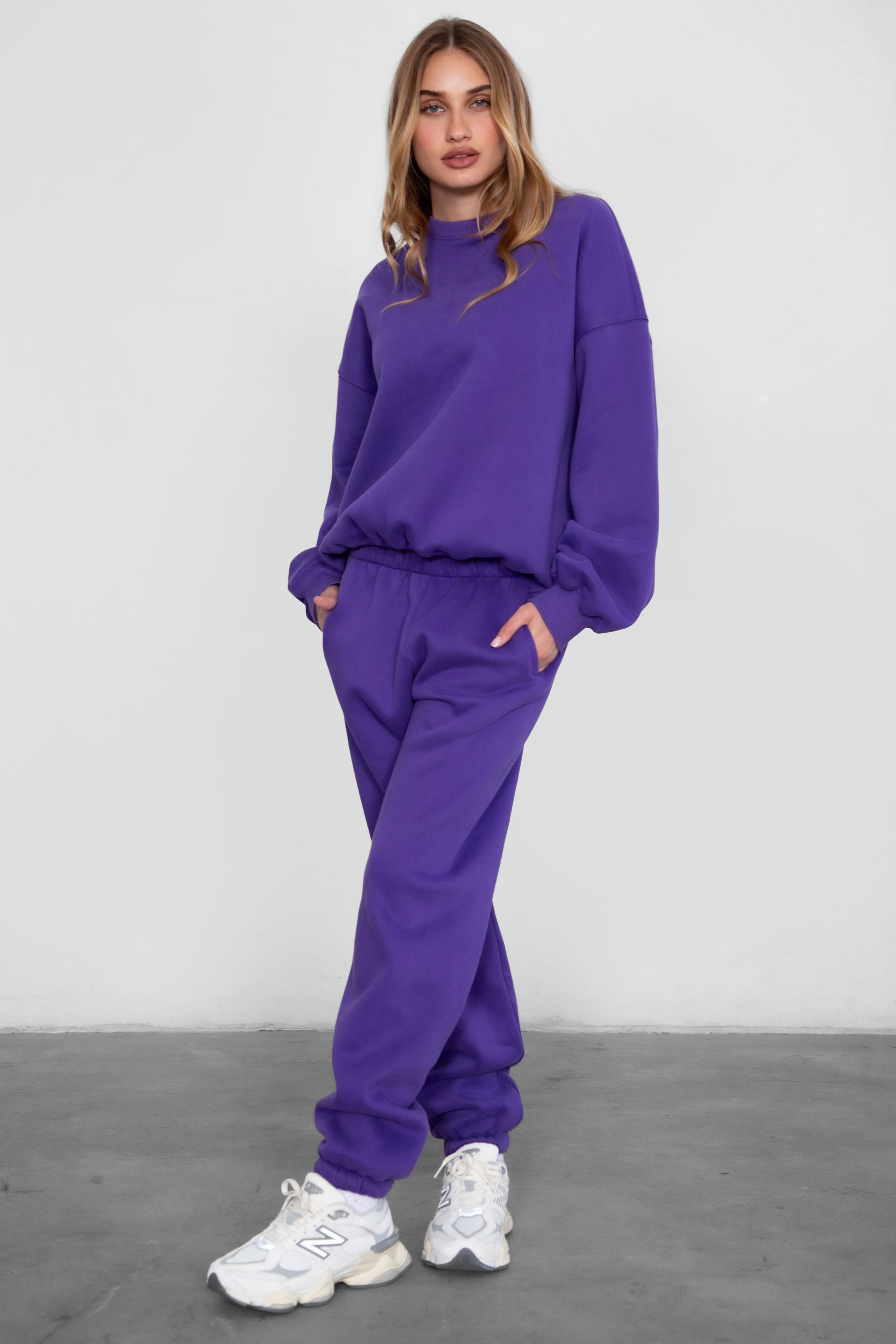 Woman wearing the TIC TOC TH28243 VARSITY purple fleece crew neck pullover sweatshirt featuring dropped shoulders, ribbed trim, and plush fleece fabric with the matching bottoms 