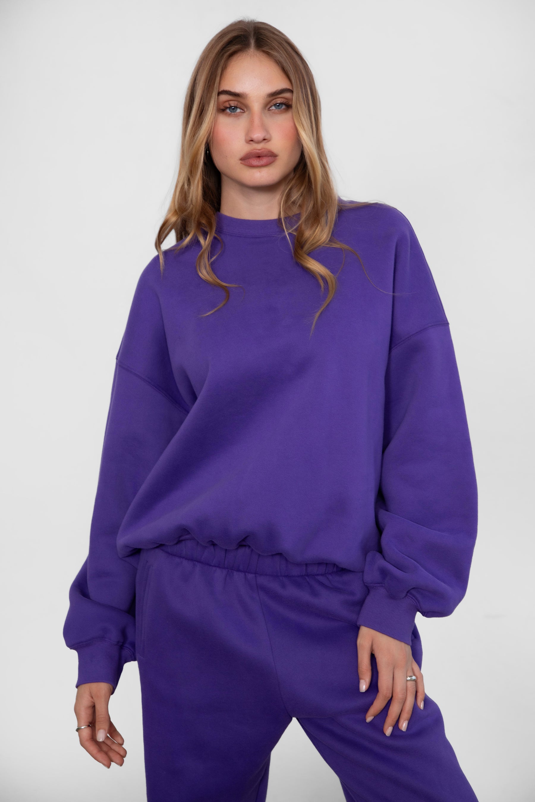 Woman wearing the TIC TOC TH28243 VARSITY purple fleece crew neck pullover sweatshirt featuring dropped shoulders, ribbed trim, and plush fleece fabric with the matching bottoms 