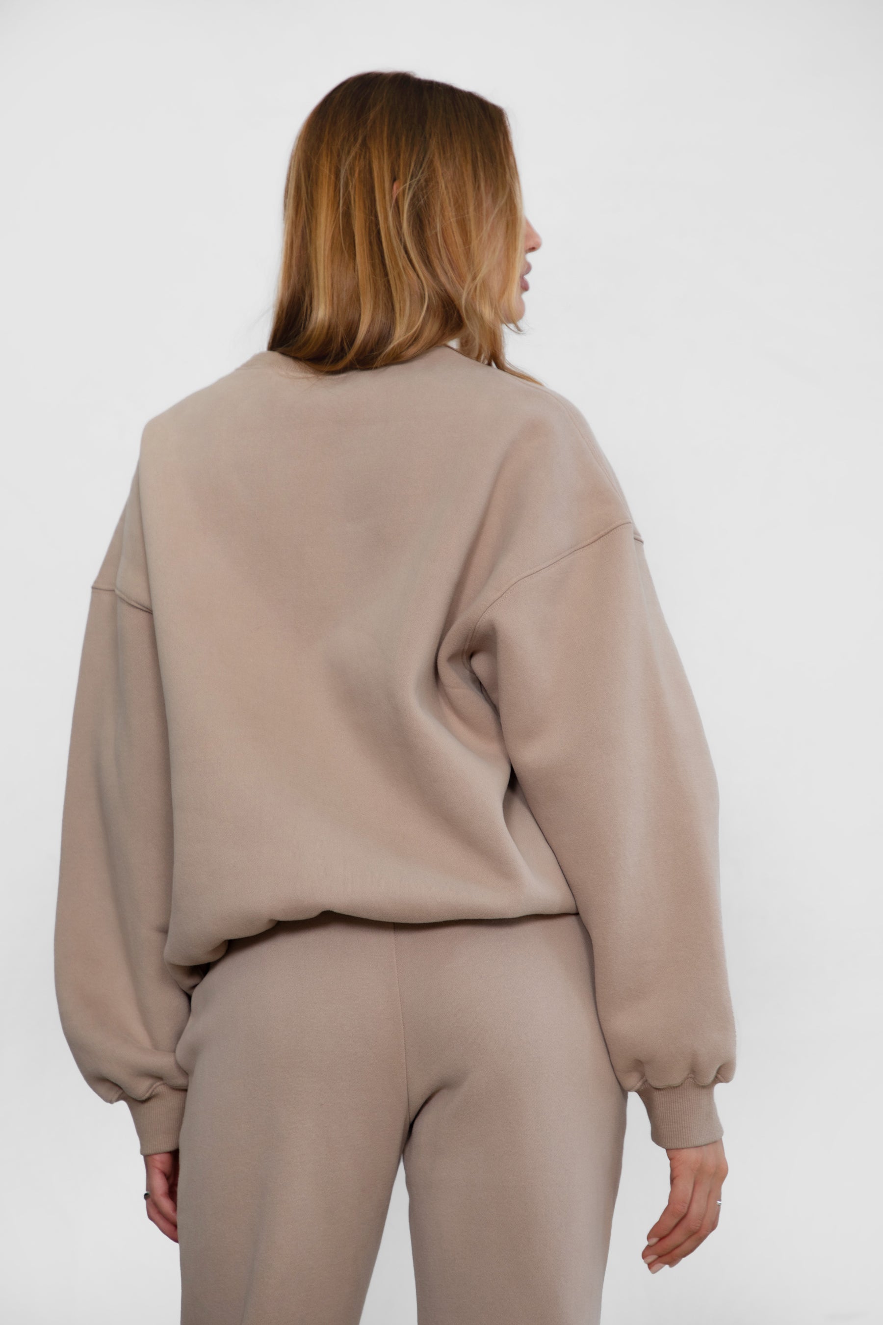 Woman wearing the TIC TOC TH28243 VARSITY taupe fleece crew neck pullover sweatshirt featuring dropped shoulders, ribbed trim, and plush fleece fabric with the matching bottoms 