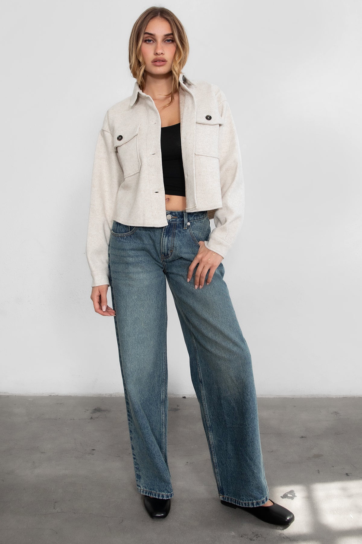 Woman wearing TIC TOC TH29147 WOOLIE faux wool cropped shacket with button front, collared neckline, and double pocket detail in color oatmeal paired with denim pants. 