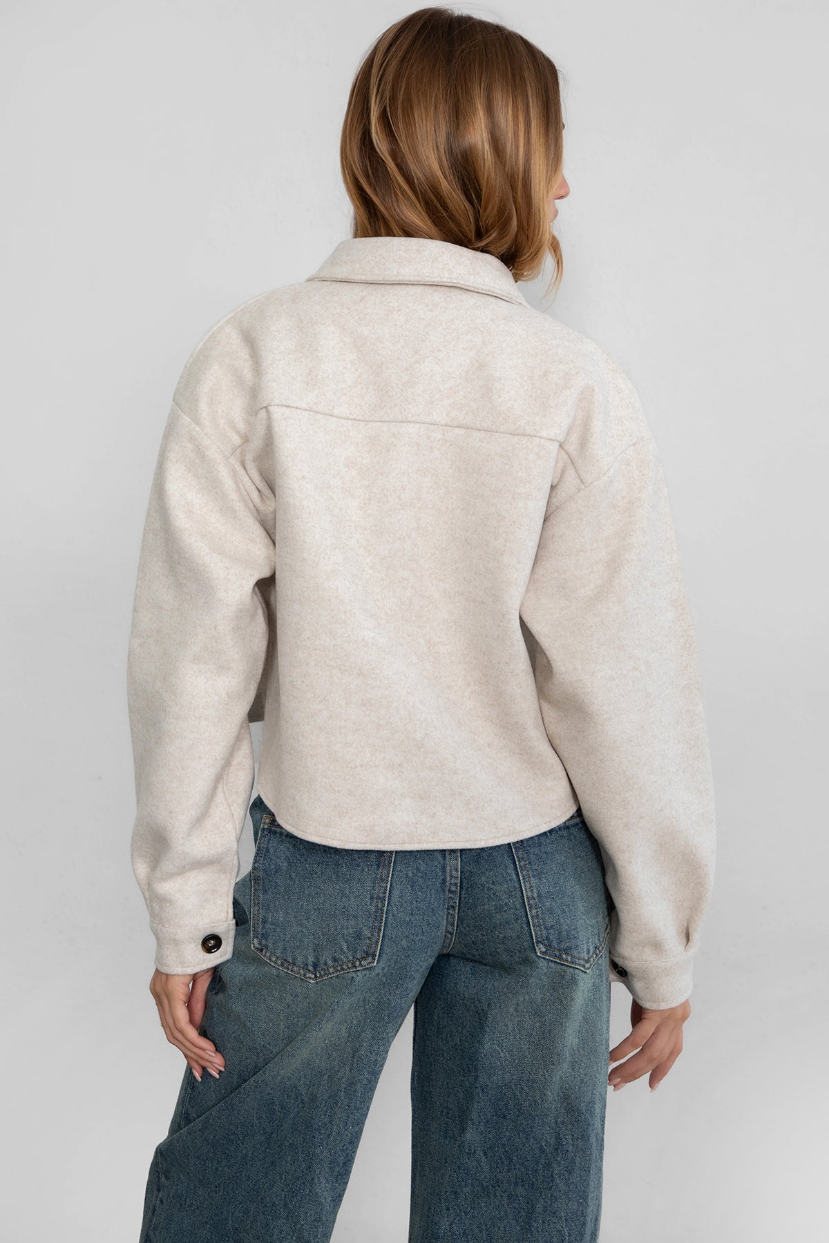 Woman wearing TIC TOC TH29147 WOOLIE faux wool cropped shacket with button front, collared neckline, and double pocket detail in color oatmeal paired with denim pants. 