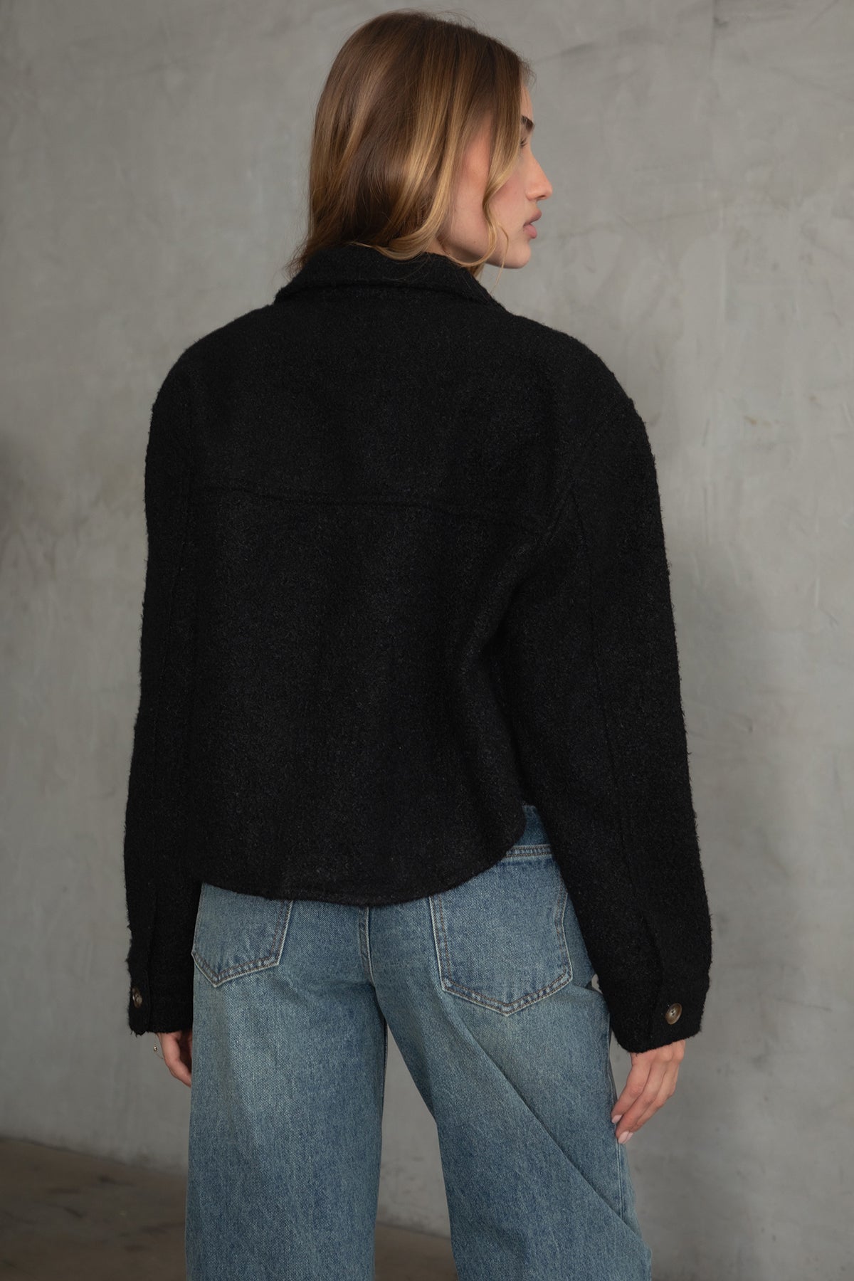 Woman wearing TIC TOC TH29288 FRAY faux sherpa cropped shacket with button front, double pockets, and collared neckline in color black paired with denim jeans