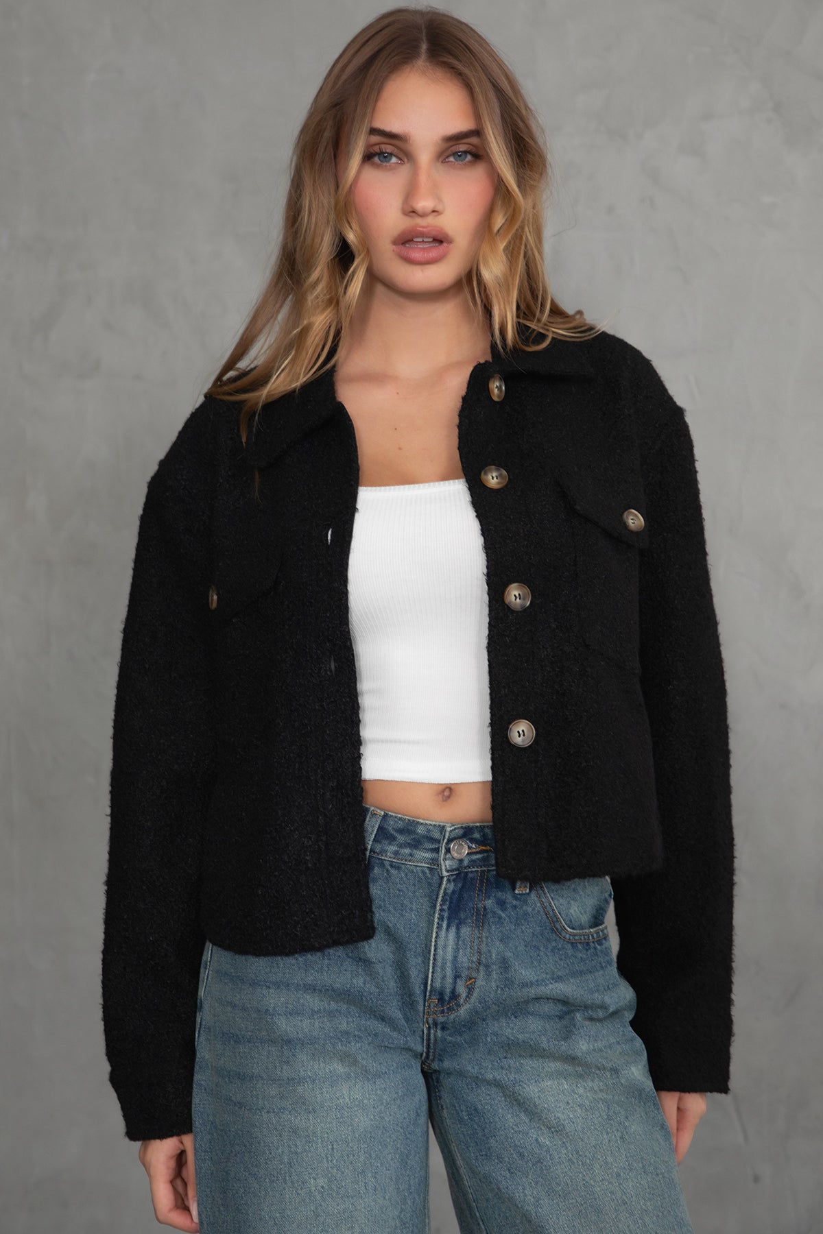 Woman wearing TIC TOC TH29288 FRAY faux sherpa cropped shacket with button front, double pockets, and collared neckline in color black paired with denim jeans