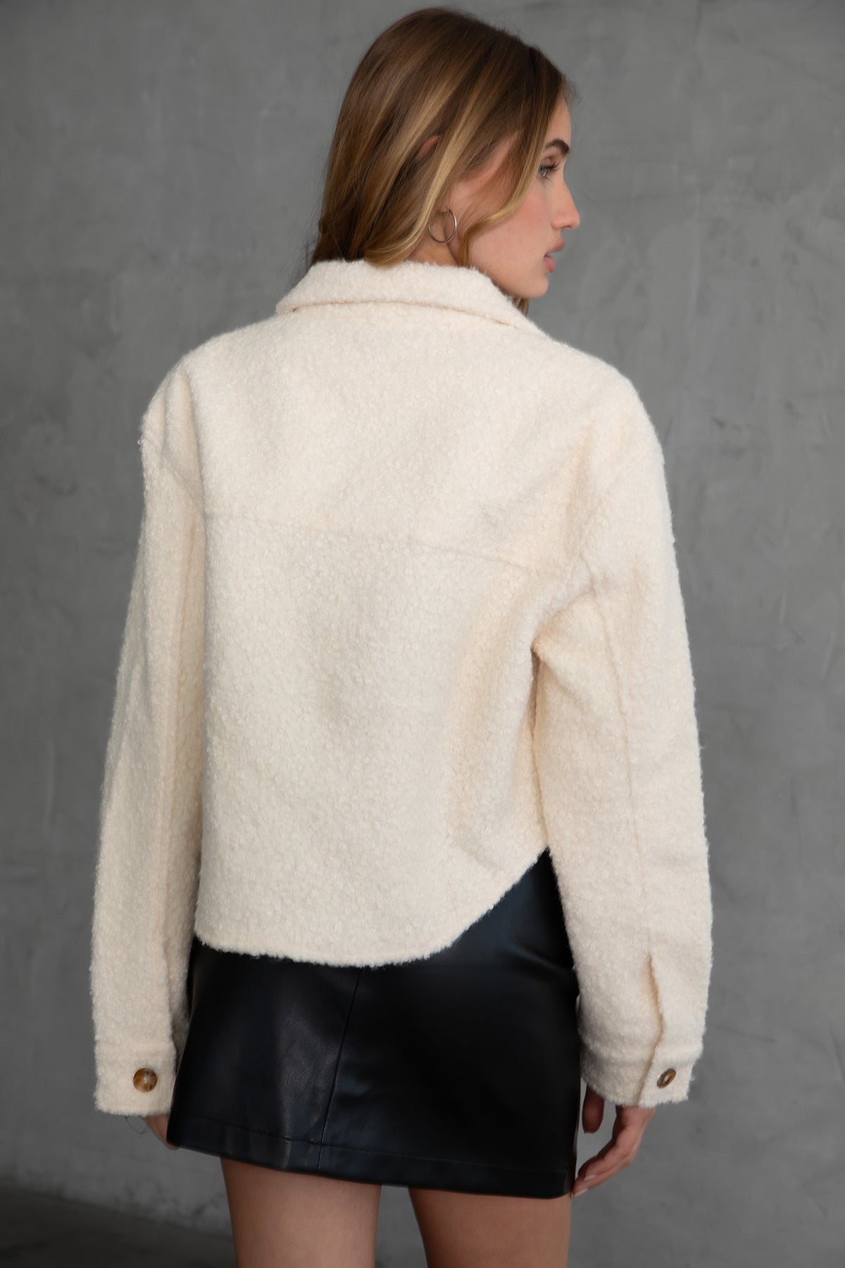 Woman wearing TIC TOC TH29288 FRAY faux sherpa cropped shacket with button front, double pockets, and collared neckline in color cream paired with a black mini skirt 