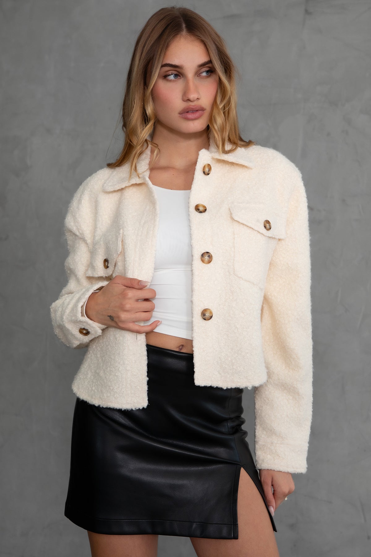 Woman wearing TIC TOC TH29288 FRAY faux sherpa cropped shacket with button front, double pockets, and collared neckline in color cream paired with a black mini skirt 