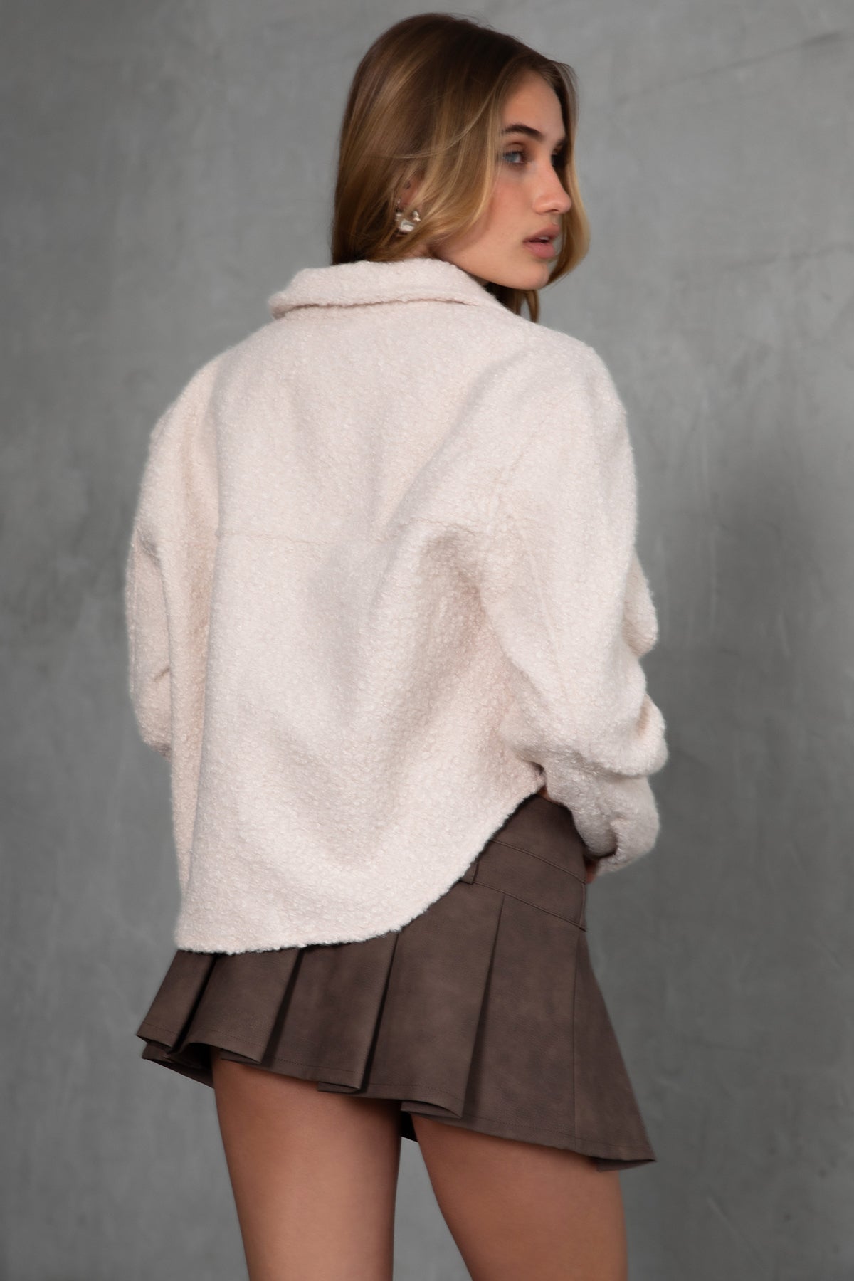 Woman wearing TIC TOC TH29288 FRAY faux sherpa cropped shacket with button front, double pockets, and collared neckline in color oatmeal paired with a mini skirt 