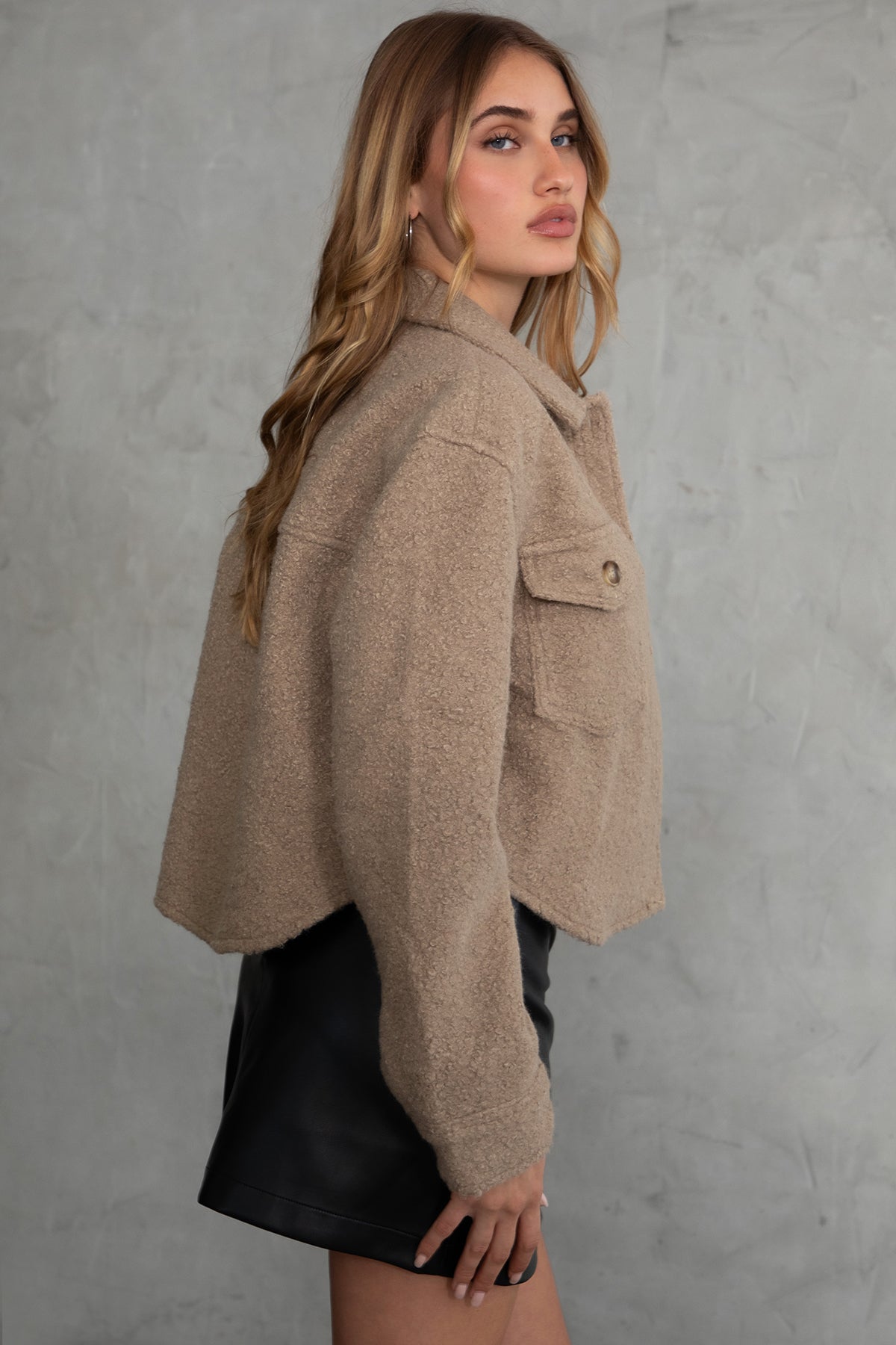 Woman wearing TIC TOC TH29288 FRAY faux sherpa cropped shacket with button front, double pockets, and collared neckline in color taupe paired with a black mini skirt 