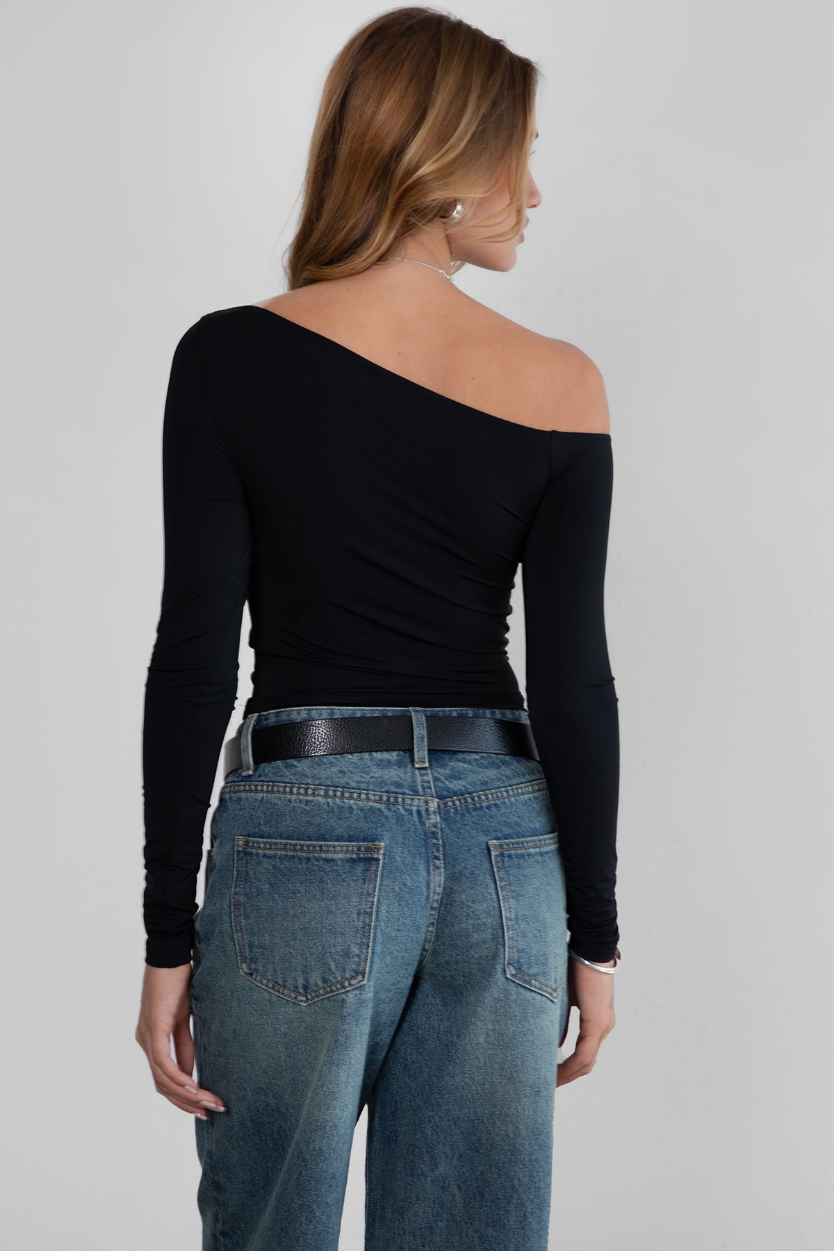 Woman wearing TIC TOC TH30538 AUDREE lightweight one-shoulder long sleeve top in slim fit stretch fabric in color black paired with dark denim blue jeans. 