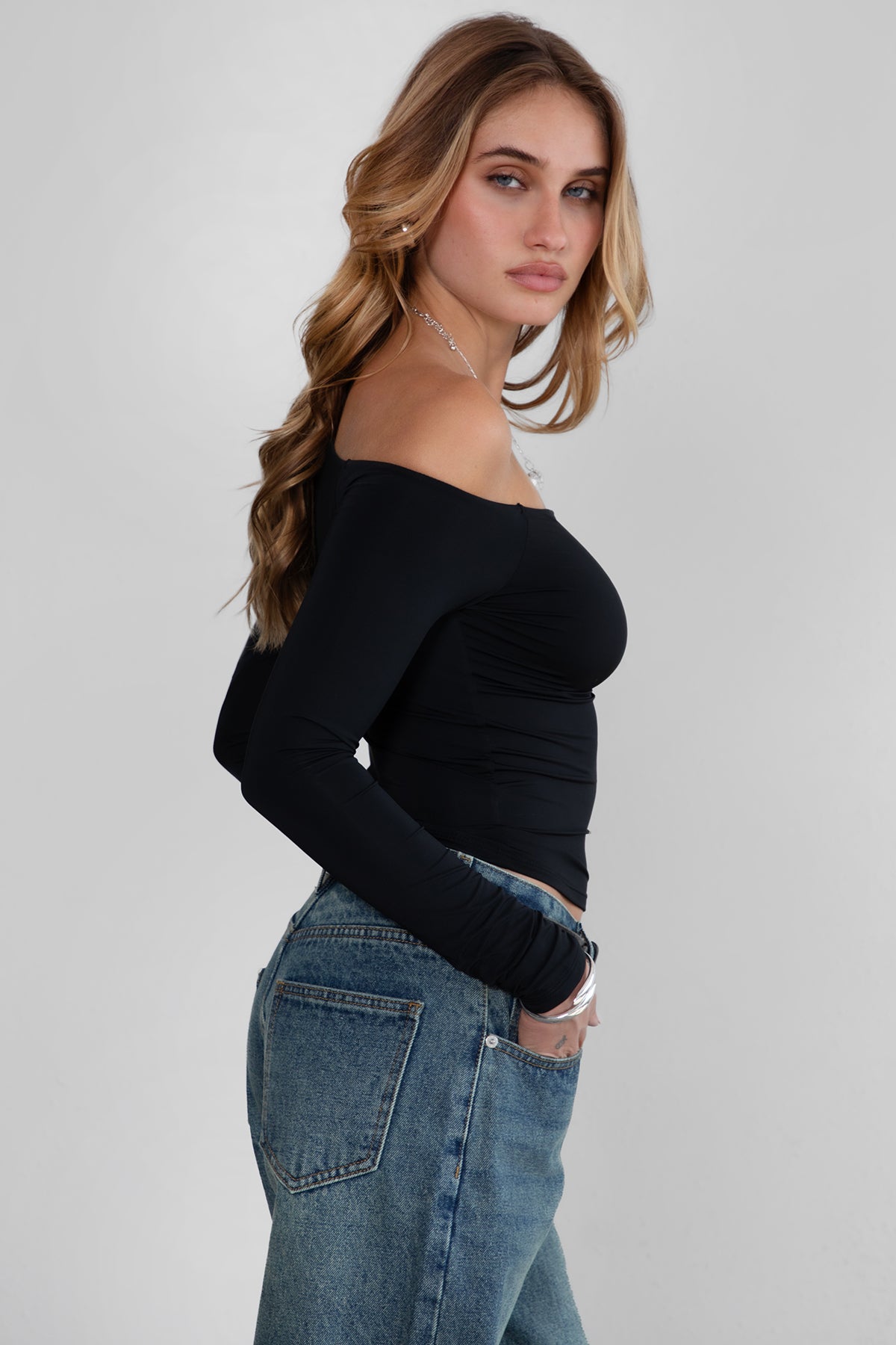 Woman wearing TIC TOC TH30538 AUDREE lightweight one-shoulder long sleeve top in slim fit stretch fabric in color black paired with dark denim blue jeans. 