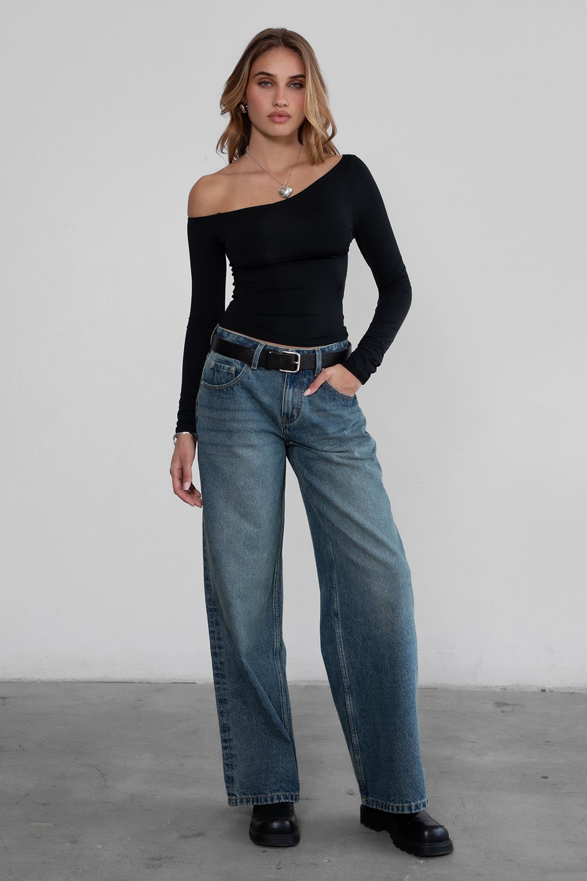 Woman wearing TIC TOC TH30538 AUDREE lightweight one-shoulder long sleeve top in slim fit stretch fabric in color black paired with dark denim blue jeans. 