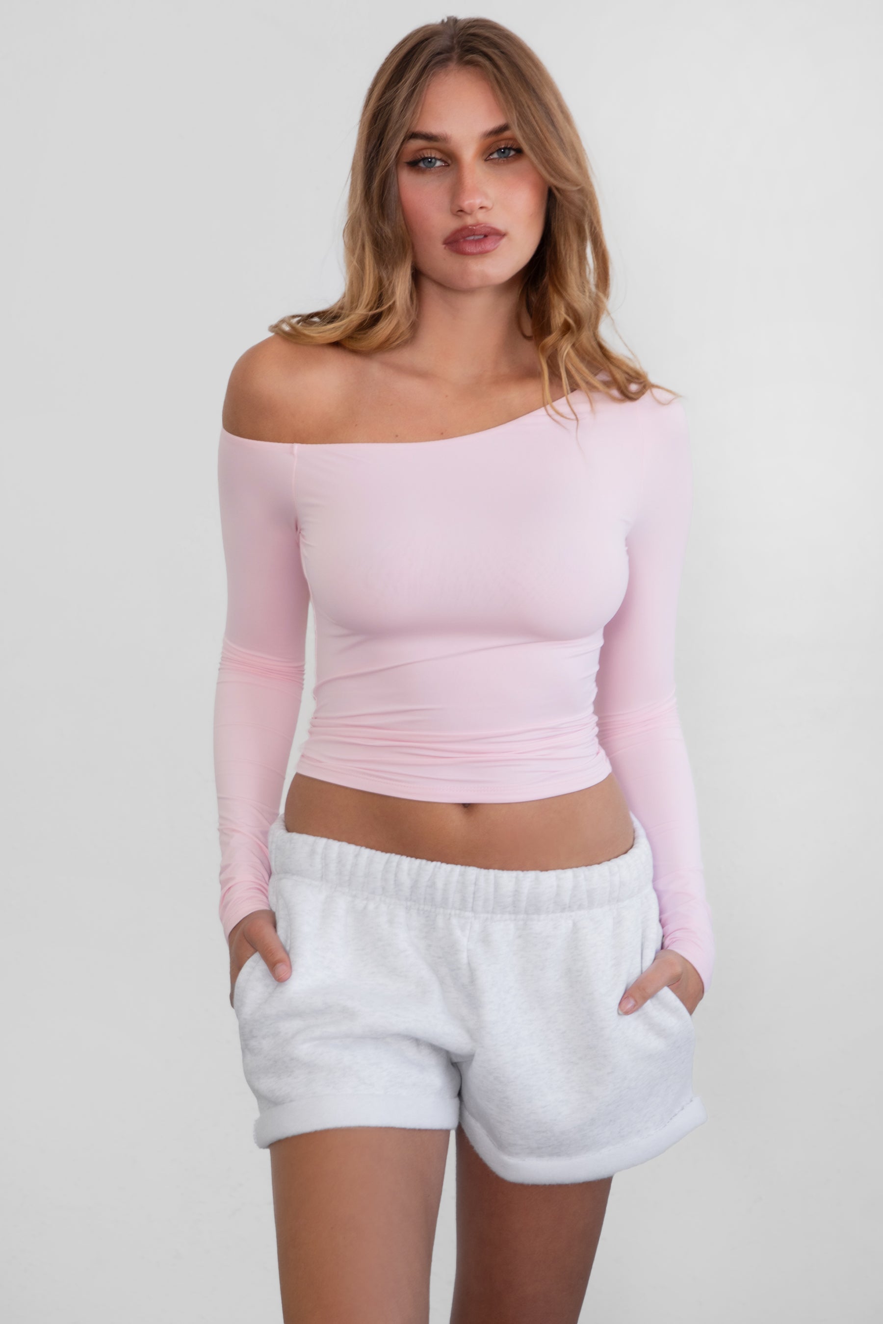 Woman wearing TIC TOC TH30538 AUDREE lightweight one-shoulder long sleeve top in slim fit stretch fabric in color blush paired with ash fleece shorts. 