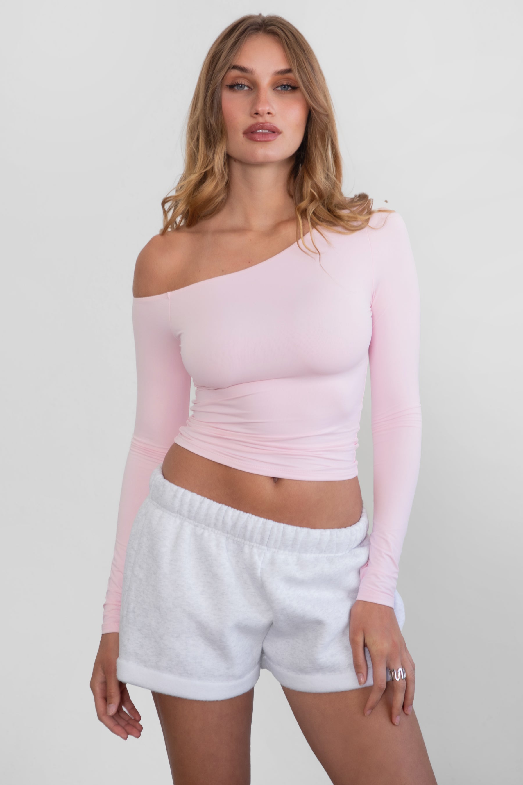 Woman wearing TIC TOC TH30538 AUDREE lightweight one-shoulder long sleeve top in slim fit stretch fabric in color blush paired with ash fleece shorts. 