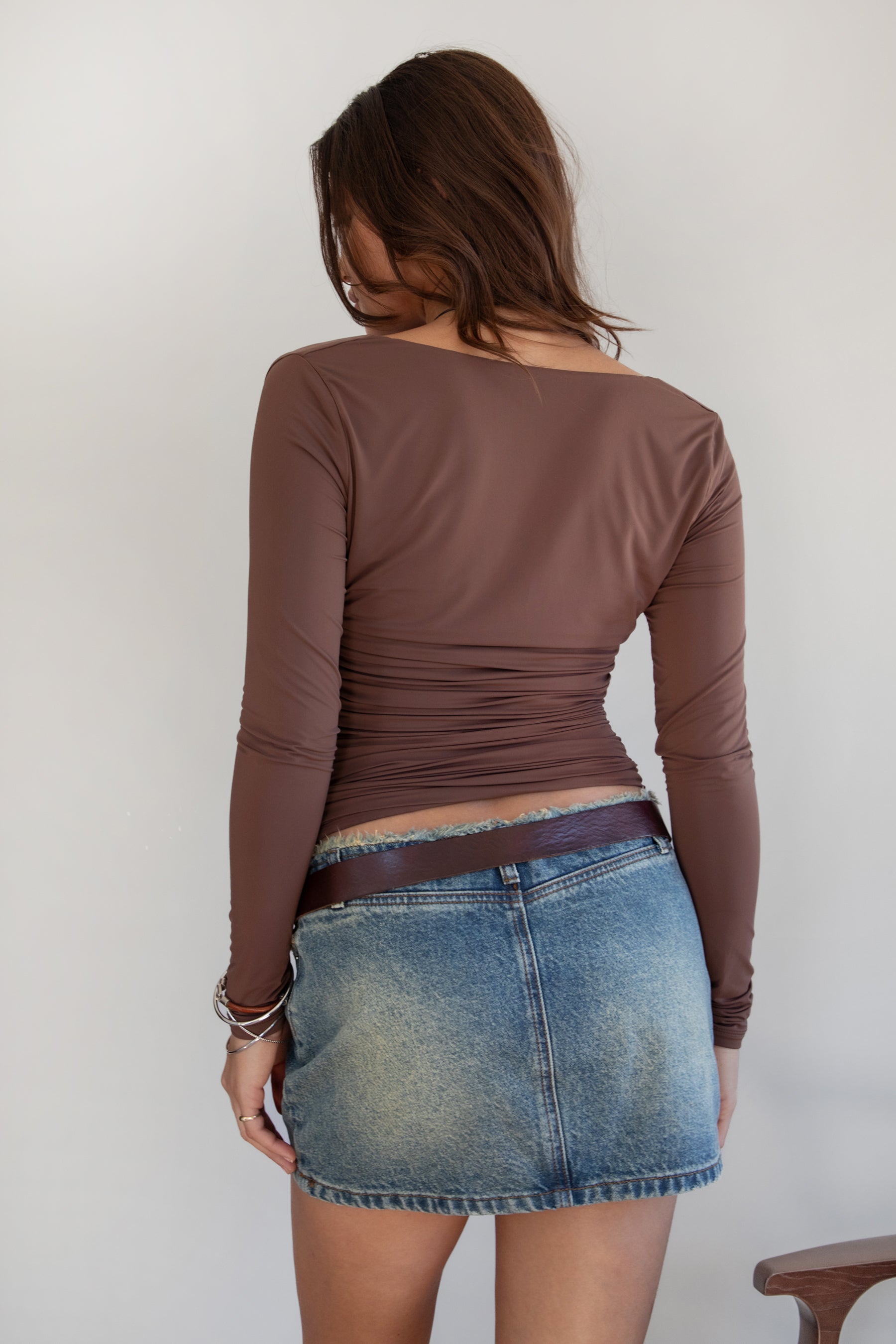 Woman wearing the TIC TOC TH31664 VELARI brown cowl neck long sleeve top featuring a draped neckline, off-the-shoulder fit, and side ruching detail paired with a denim mini skirt