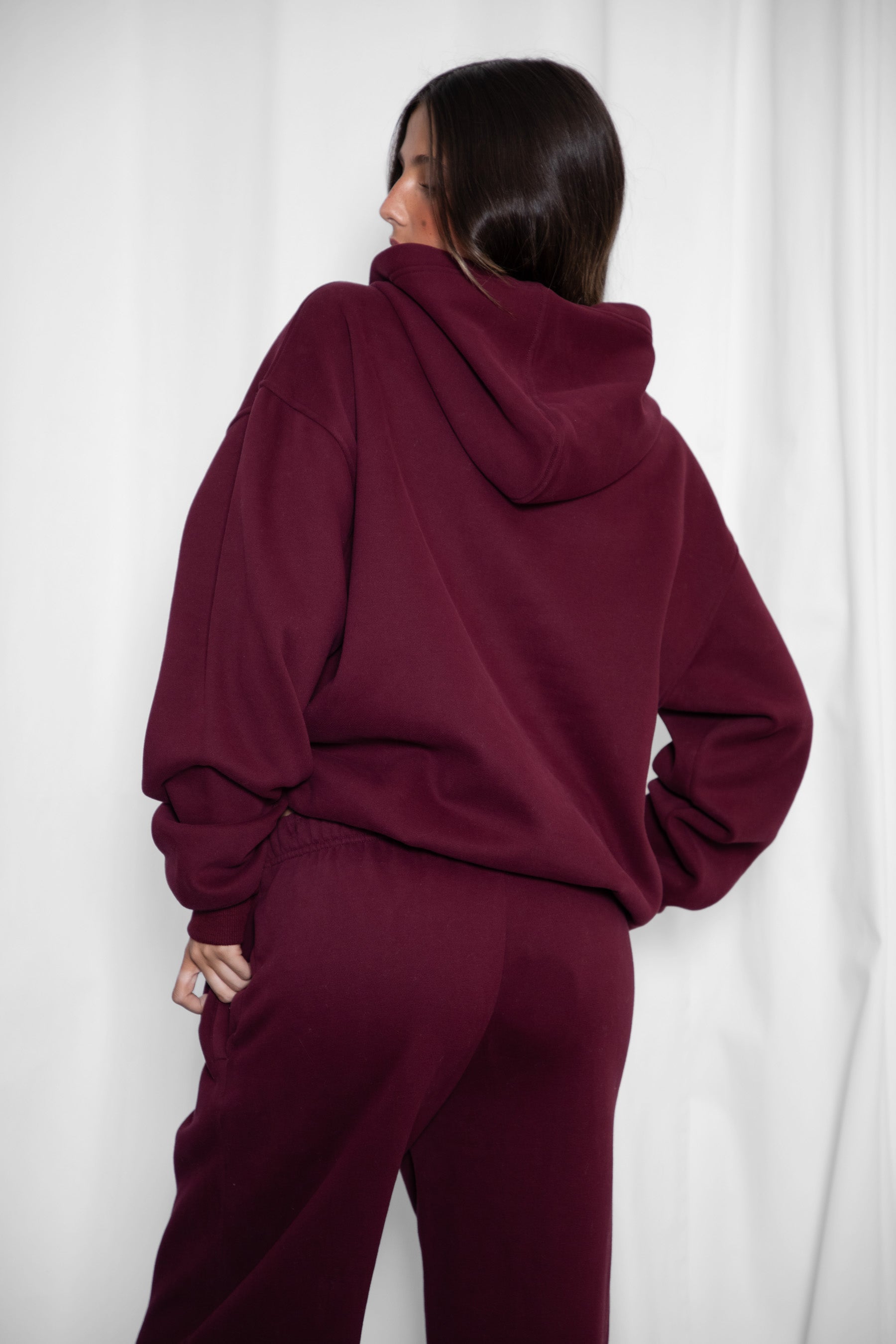 A female model wearing a black cherry oversized hoodie with a hood, long sleeves paired with matching bottoms. 