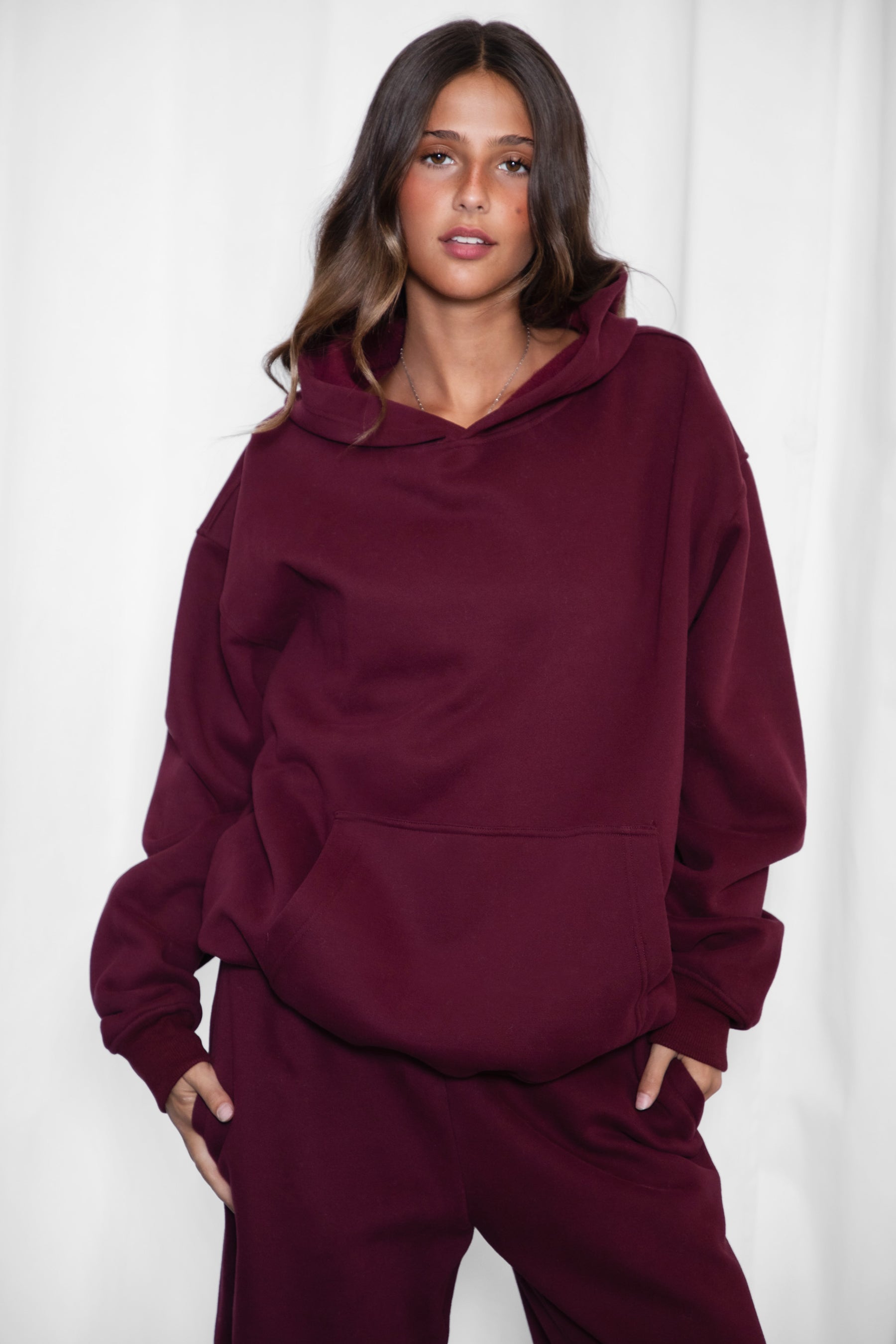 A female model wearing a black cherry oversized hoodie with a hood, long sleeves paired with matching bottoms. 