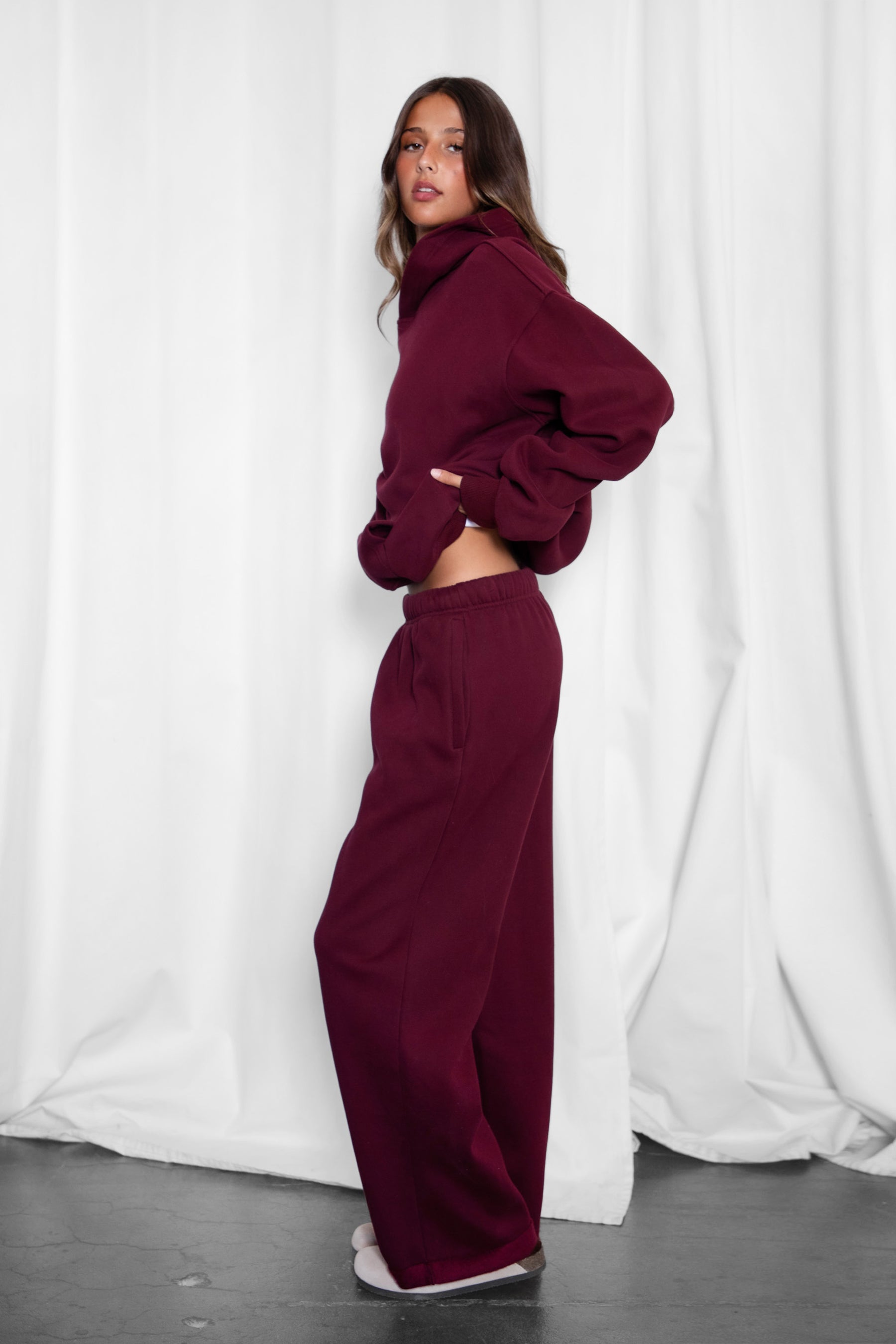 A female model wearing a black cherry oversized hoodie with a hood, long sleeves paired with matching bottoms. 