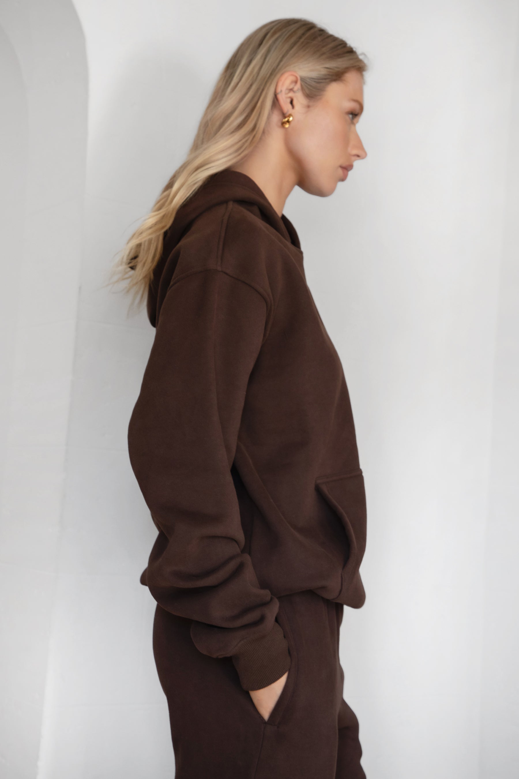 Person wearing a brown hoodie and pants against a white background