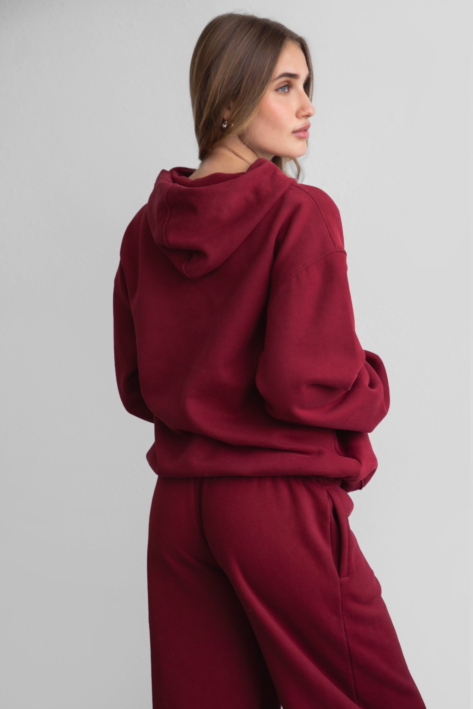 A female model wearing a maroonoversized hoodie with a hood, long sleeves paired with matching bottoms. 