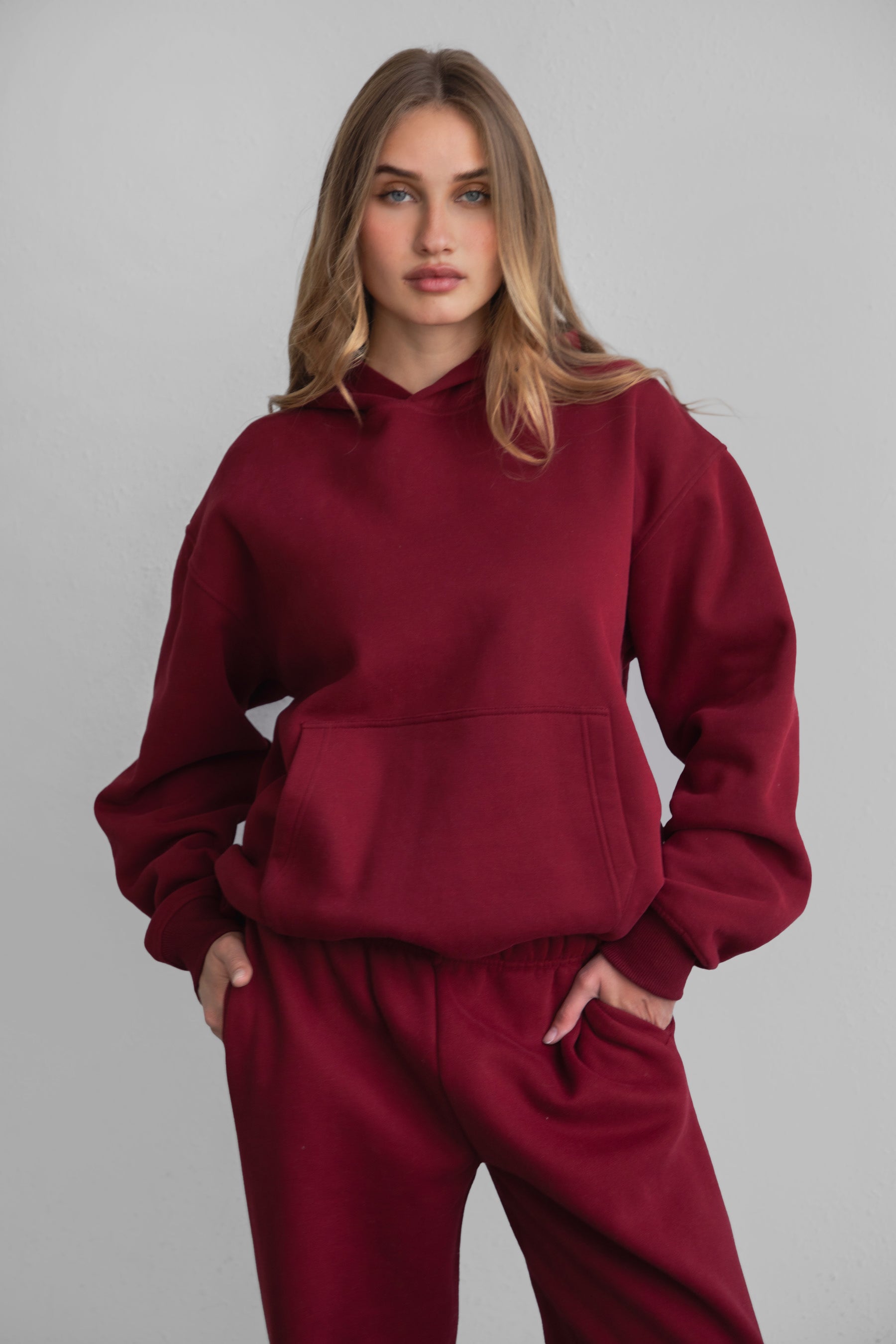 A female model wearing a maroonoversized hoodie with a hood, long sleeves paired with matching bottoms. 