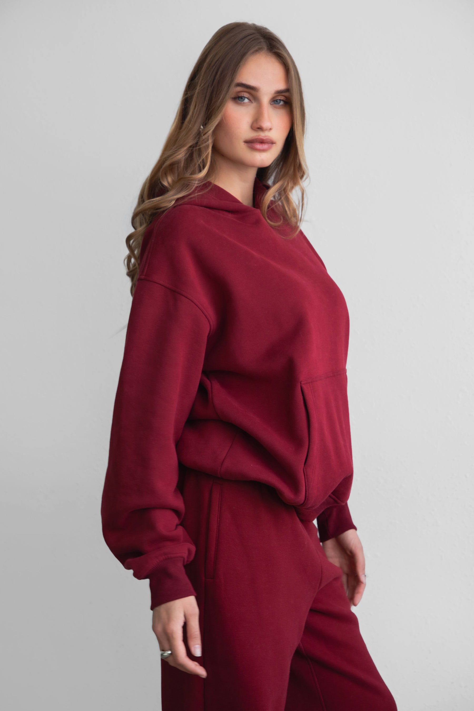A female model wearing a maroonoversized hoodie with a hood, long sleeves paired with matching bottoms. 