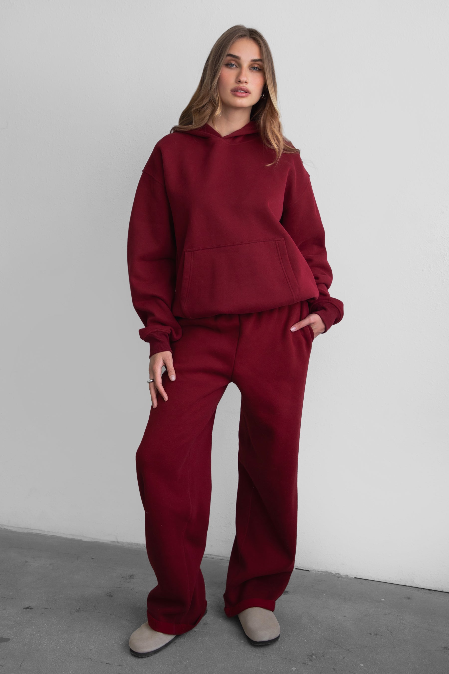 A female model wearing a maroonoversized hoodie with a hood, long sleeves paired with matching bottoms. 