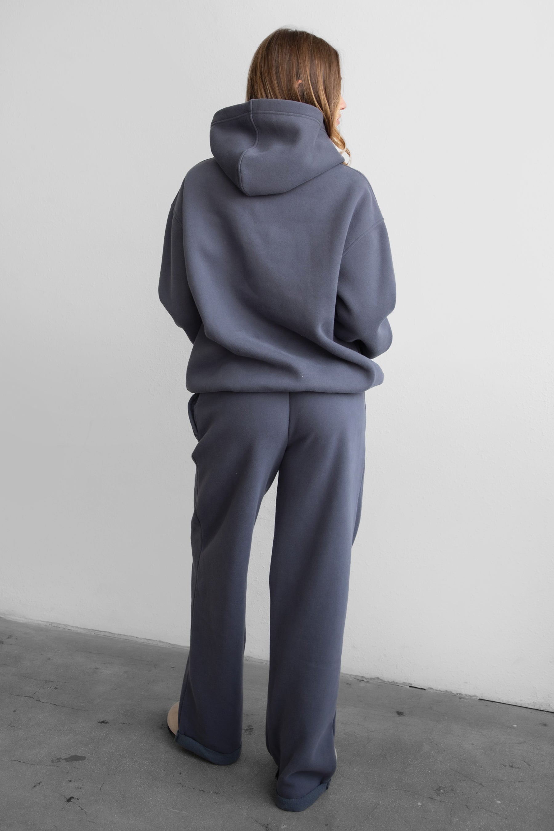 A female model wearing a steel grey oversized hoodie with a hood, long sleeves paired with matching bottoms. 