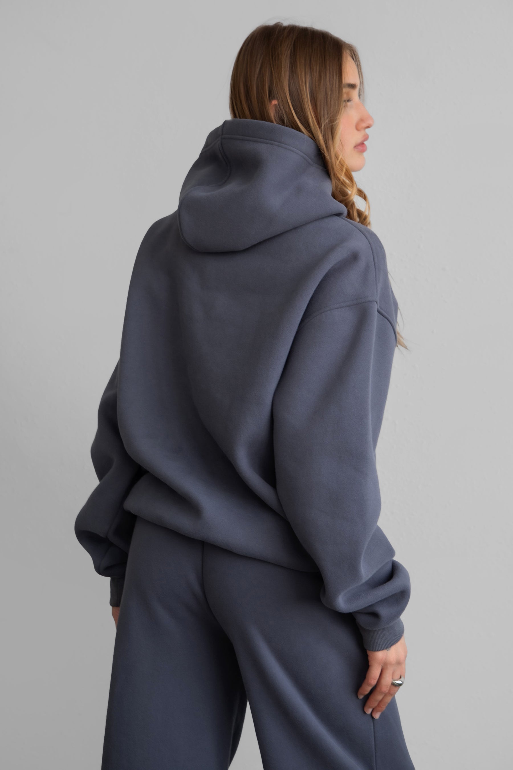A female model wearing a steel grey oversized hoodie with a hood, long sleeves paired with matching bottoms. 