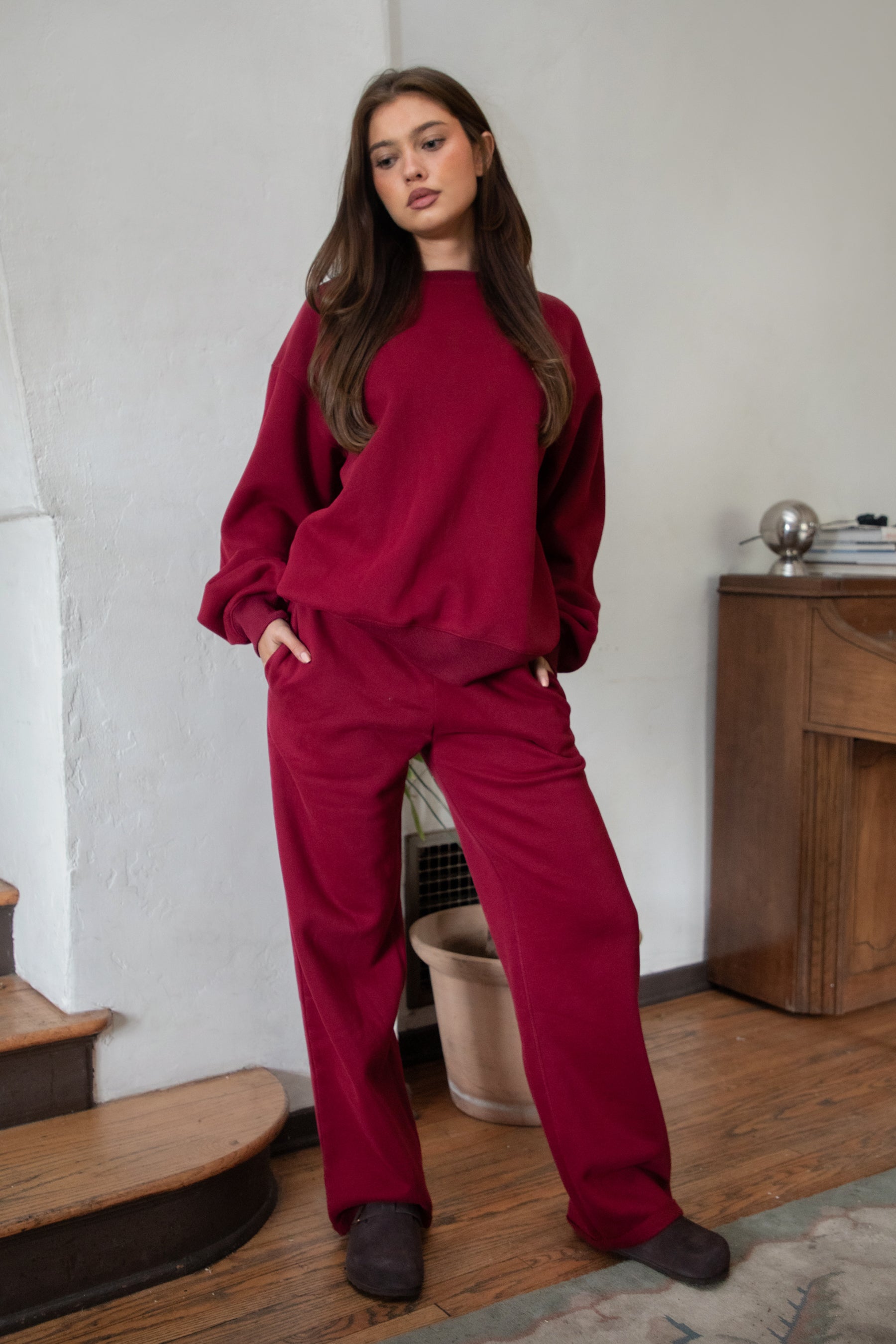 Woman wearing the TIC TOC TJ31656 LANI maroon color fleece crew neck pullover sweatshirt featuring dropped shoulders, ribbed trim, and cozy fleece fabric with the matching bottoms indoors. 